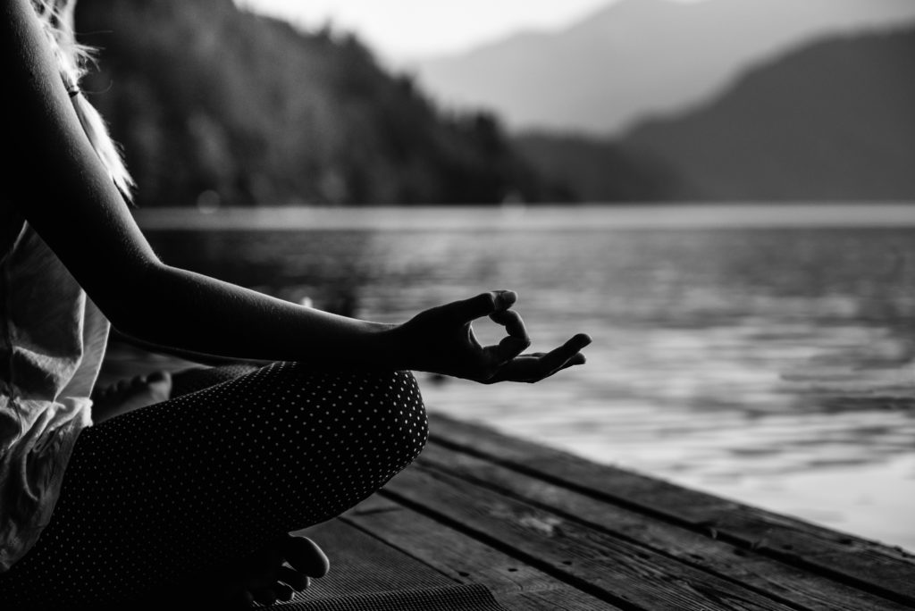 Young woman doing yoga by the lake, relaxing in lotus pose. Black and white image, focus on hand